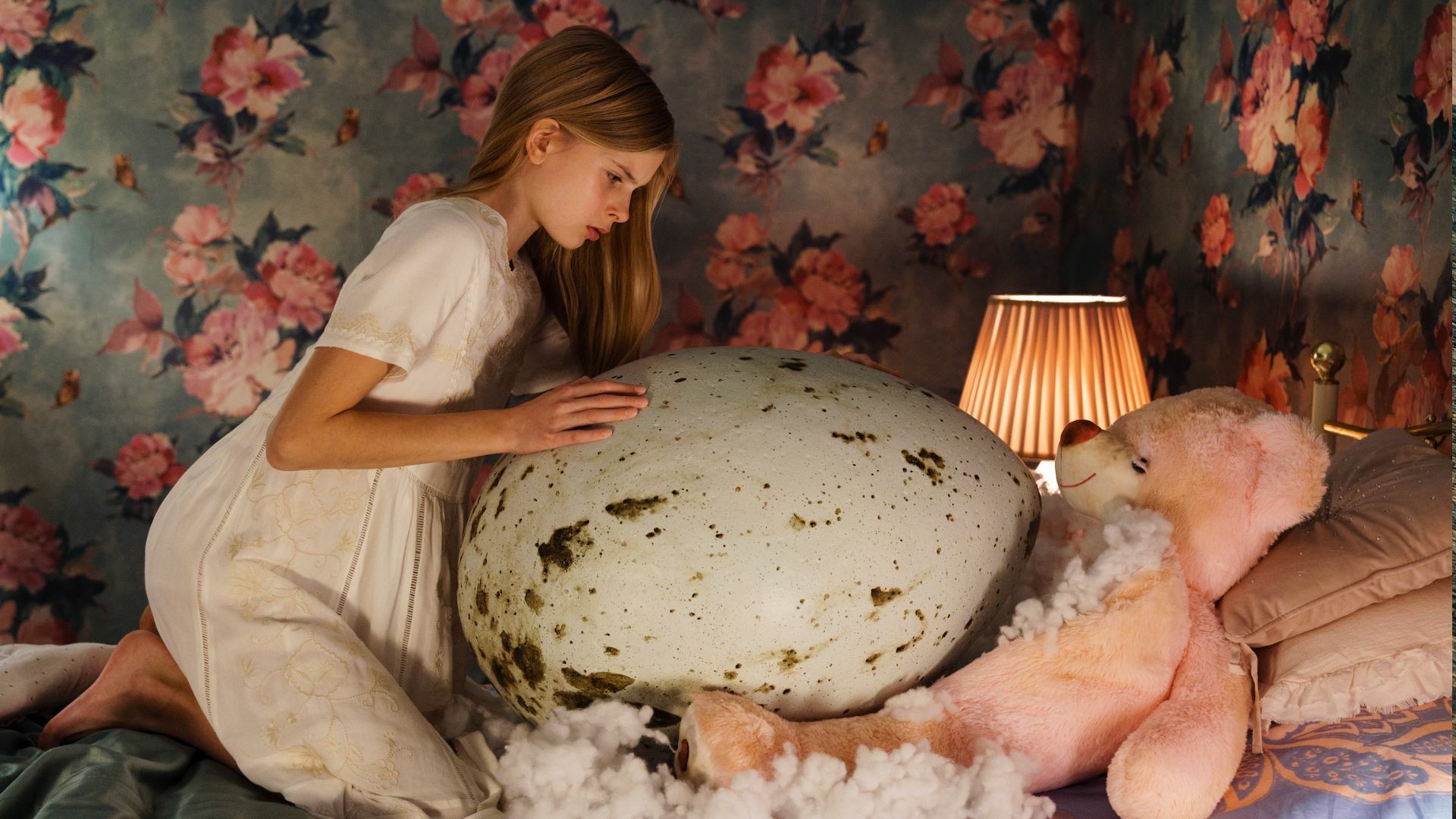 A young girl hovers over a very large egg.
