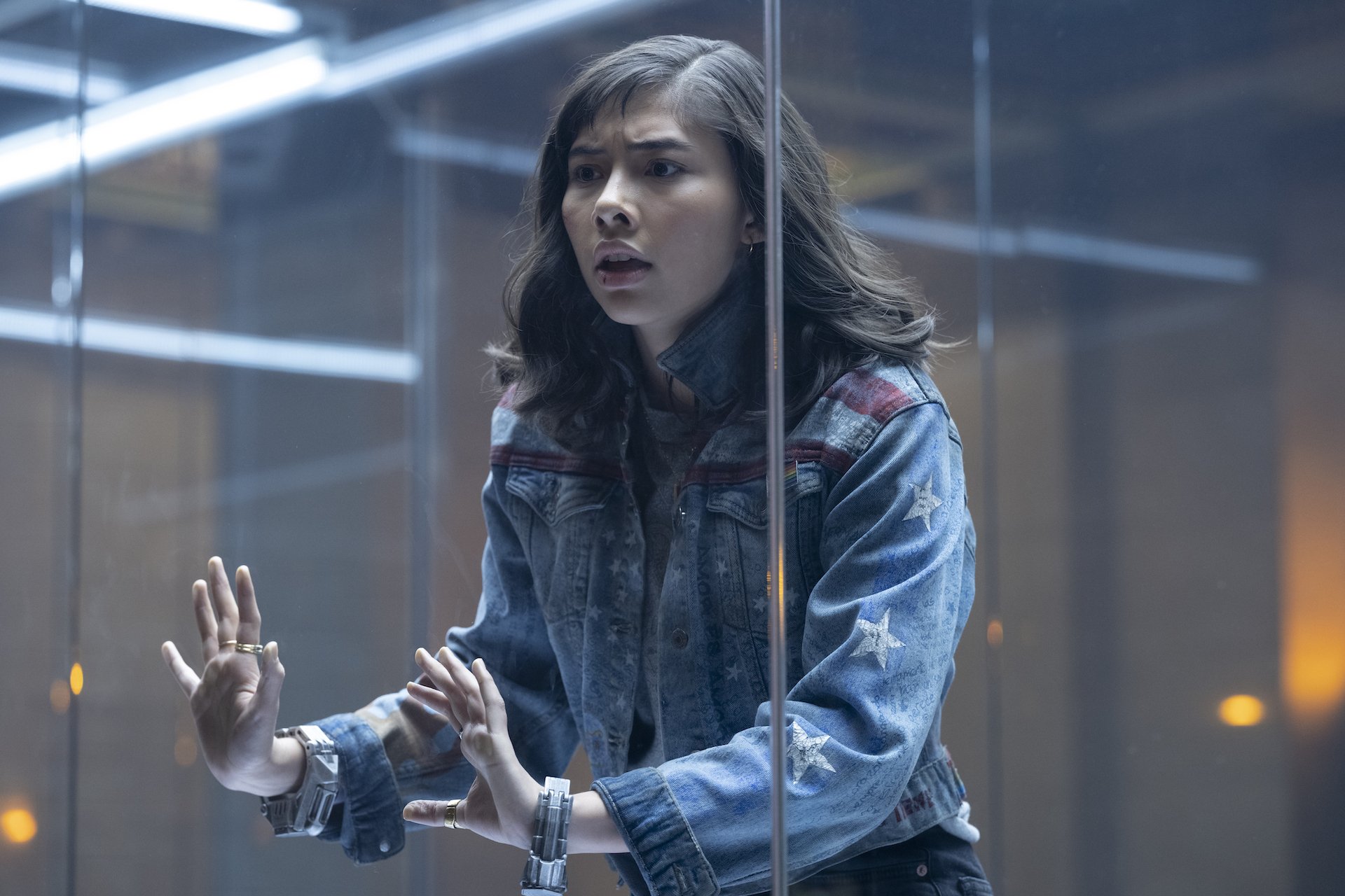 A young girl in a denim jacket trapped in a glass cage.