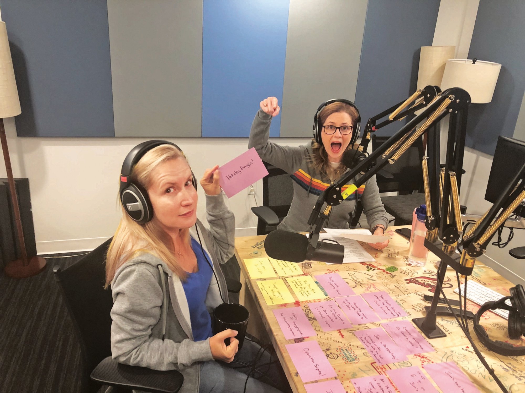 Two women (Jenna Fischer and Angela Kinsey) sitting in a recording studio in front of microphones.