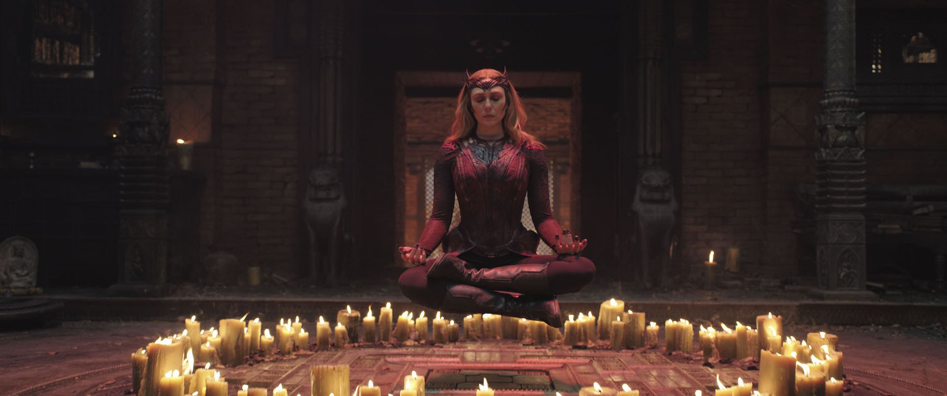 A woman in a red witch costume floating inside a ring of candles.