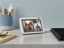 a glacier white echo show 7 sitting on a countertop next to a stove, a cutting board, and a jar of cooking utensils