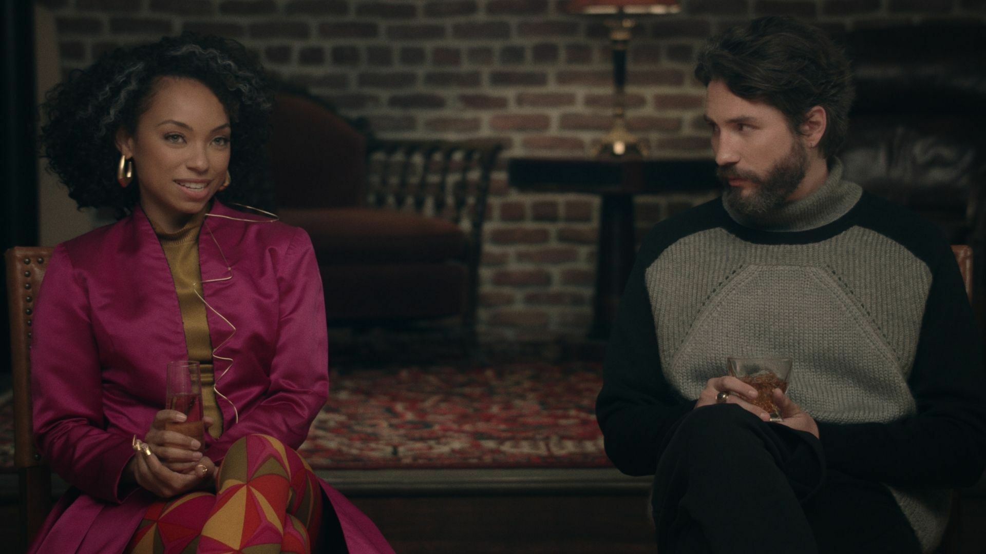 A Black woman holds a drink, sitting next to a white man who is also holding a drink, from "Dear White People"