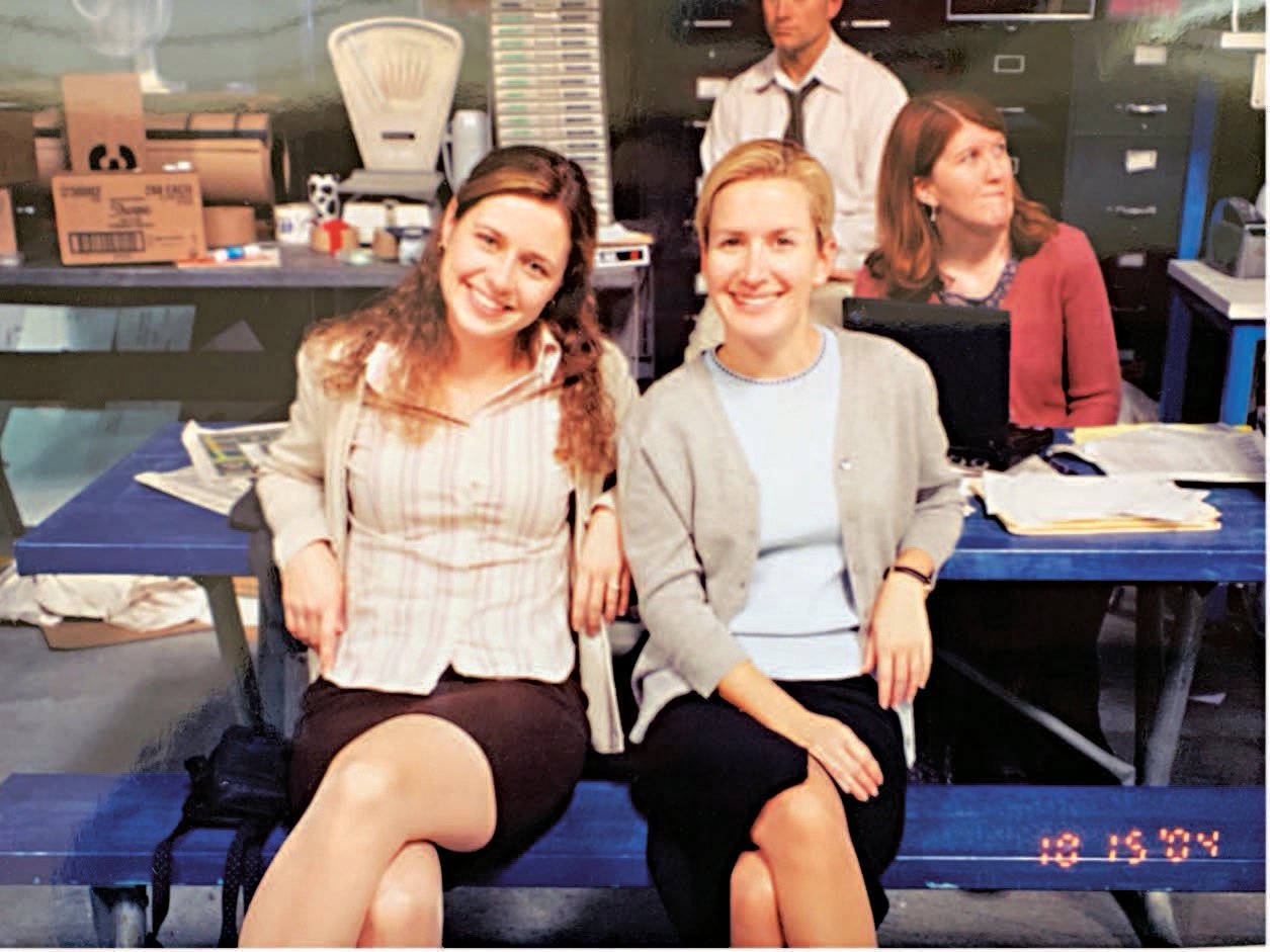 Two women (Jenna Fischer and Angela Kinsey) sitting together on a blue picnic bench.