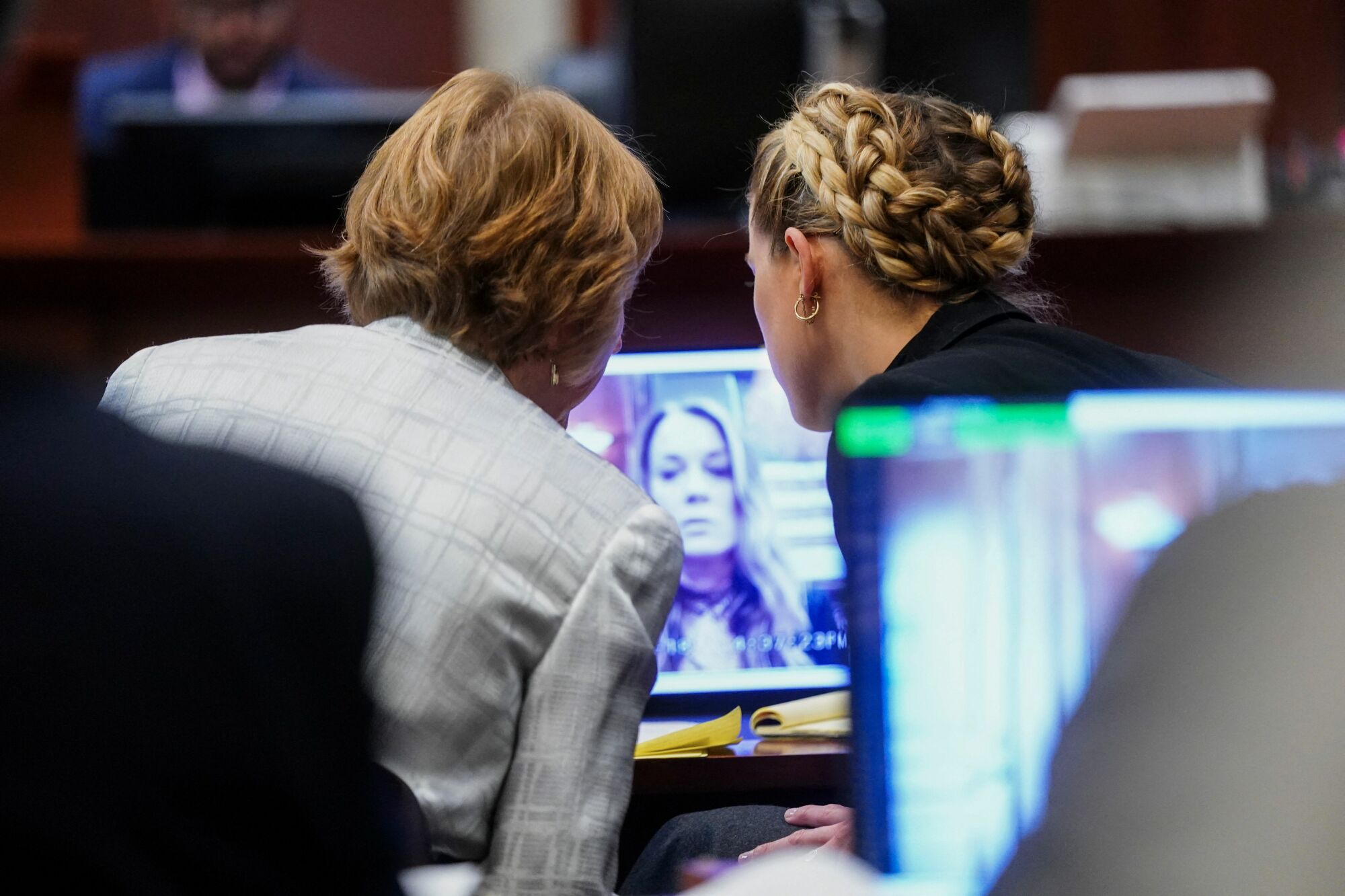 Heard and her attorney photographed at their desk in court from behind, watching a video of James on the computer screen in front of them.