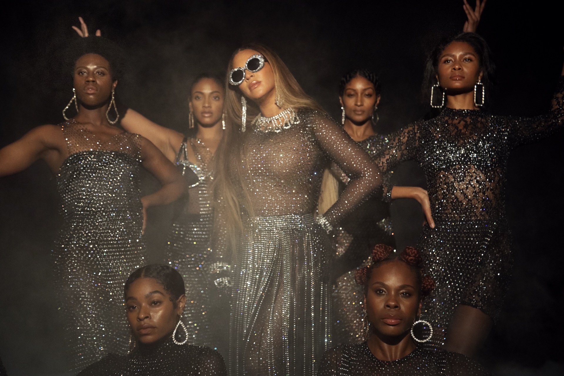 A group of Black women in sequined gowns standing behind Beyoncé.