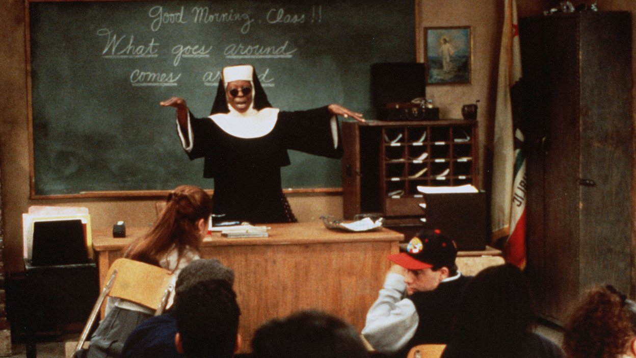 Whoopi Goldberg in a nun's habit at the front of a Catholic school classroom.