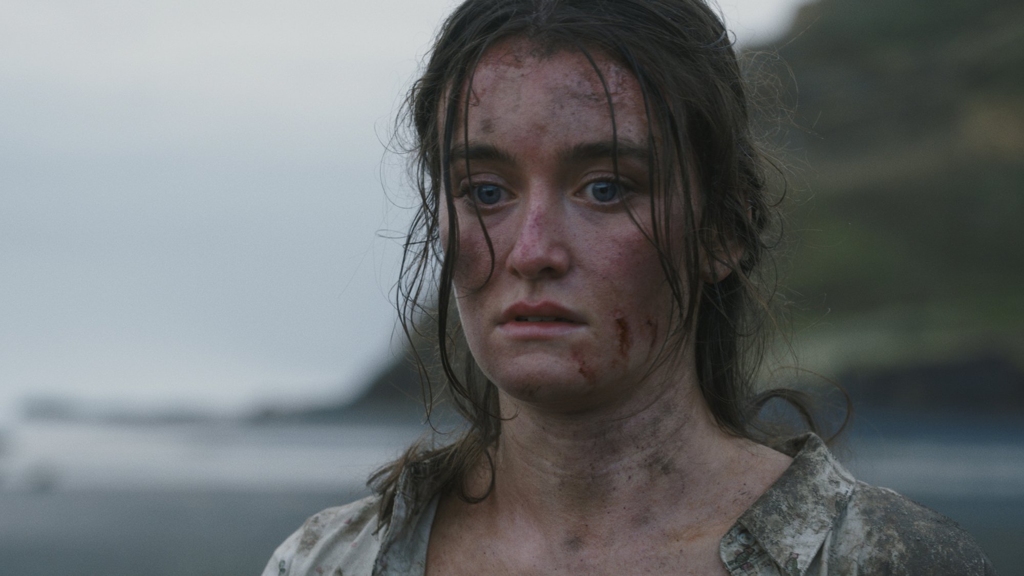 A girl with blood and dirt on her face on a beach on a tropical island.