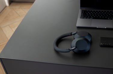 black Sony WH-1000XM5 Headphones sitting on a desk next to a laptop and a smartphone