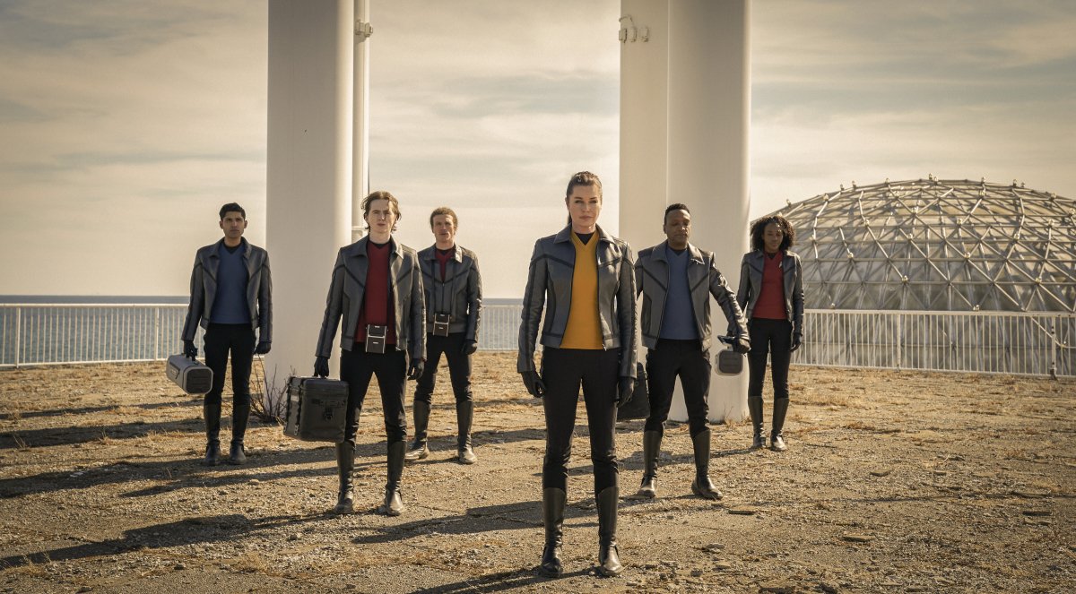 A group of seven people in red, yellow, and blue shirts stand outside with a dome in the background.