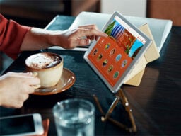 Hand touching tablet showing language-learning screen with other hand holding coffee