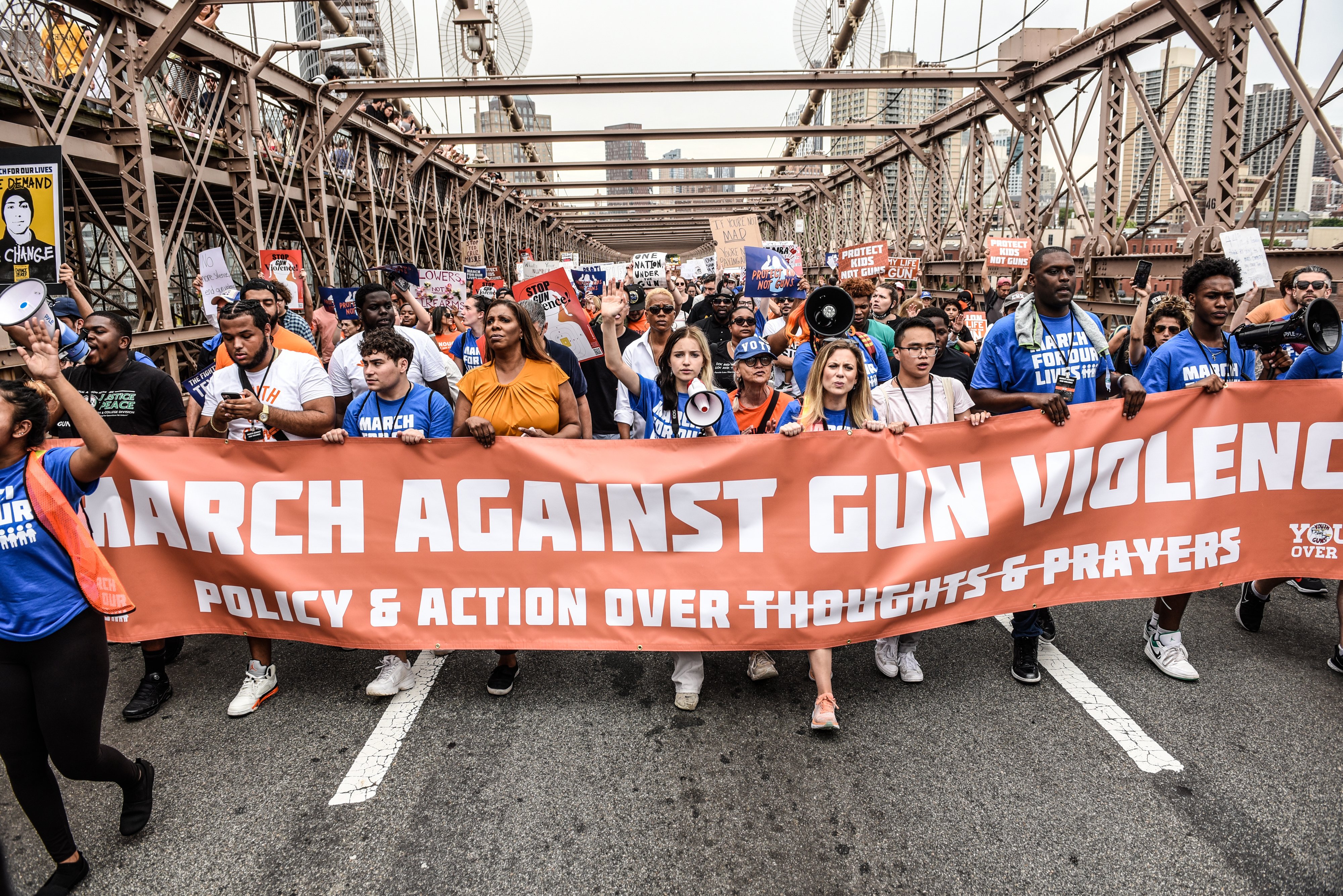 protestors crossing brooklyn bridge with orange march for our lives banner