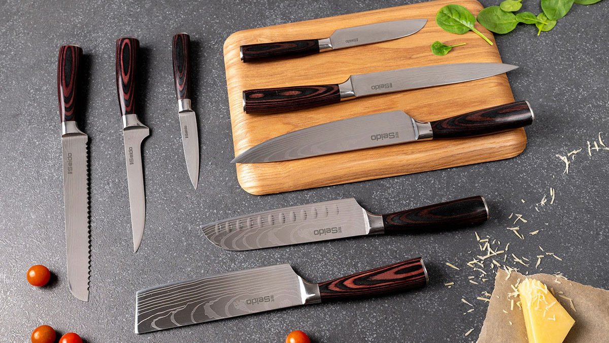 Set of eight silver knives with wooden handles on chopping board and table with cheese and cherry tomatoes