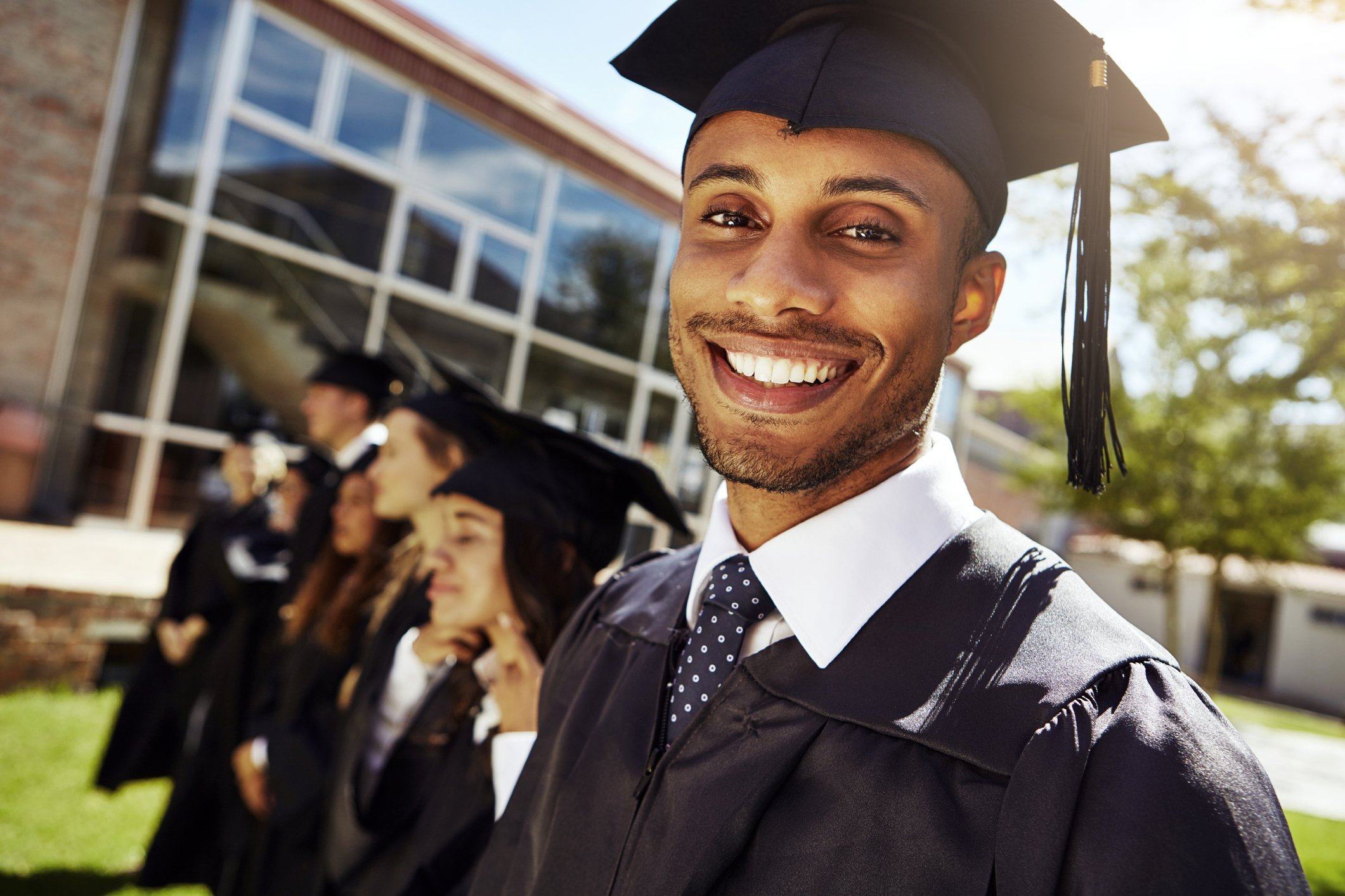group of students at graduation with one young man smiling directly at the camera