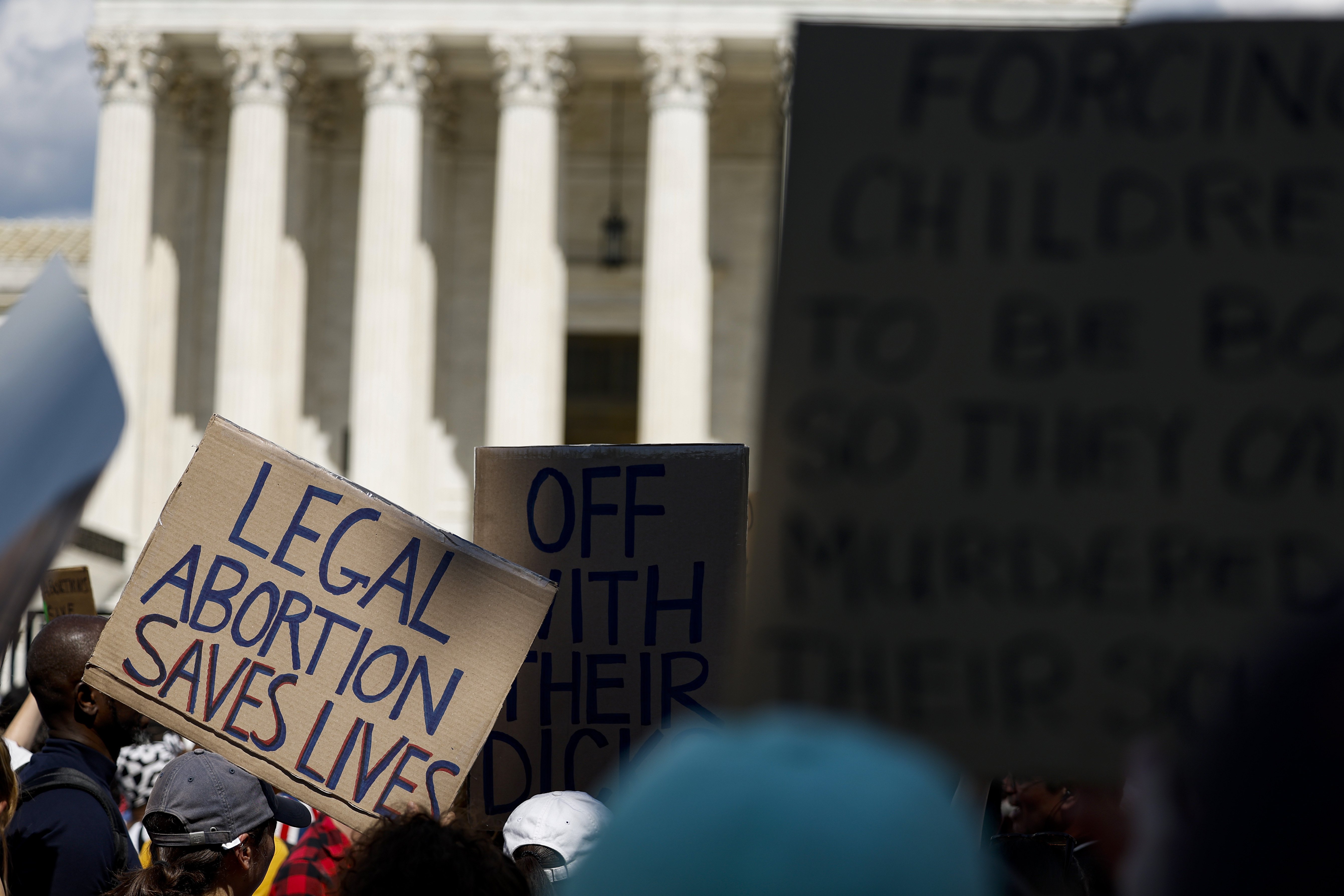 Protestors stand outside of the U.S. Supreme Court. One holds up a sign reading,