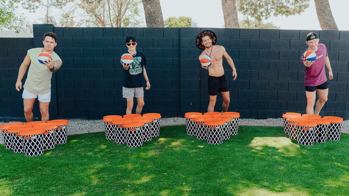 Four people behind basketball hoop-patterned bins throwing basketballs into them