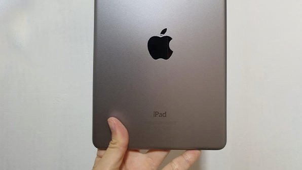 Hand holding up grey ipad from the back