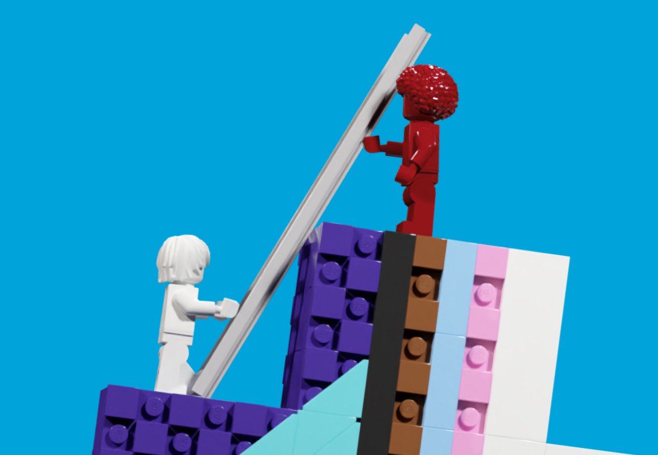 Two LEGO figures stand on a set of blocks featuring the transgender flag colors.