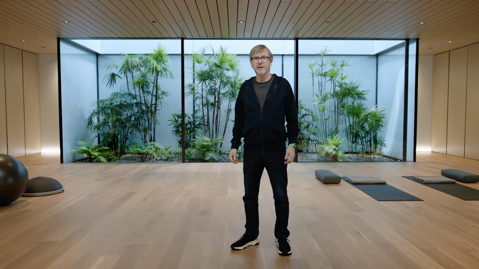 Kevin Lynch stands in a yoga studio in front of an atrium with trees.