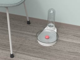Clear water dish with orange ball in the middle and tube of a dispenser behind