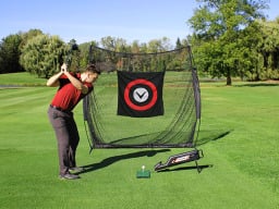 Person swinging golf club towards ball aimed at net outdoors