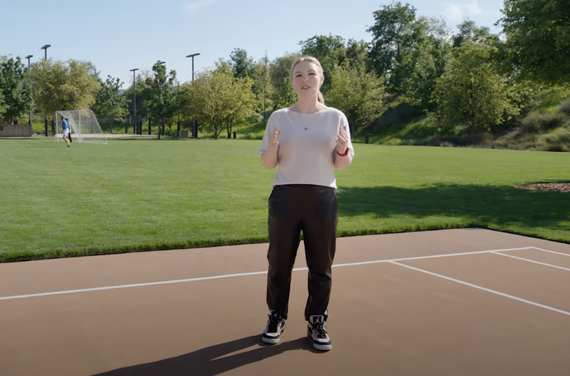 Rubie Edmondson stands in a white tee, pleather black pants, a red Apple watch, and black and white high-top Air Jordans.