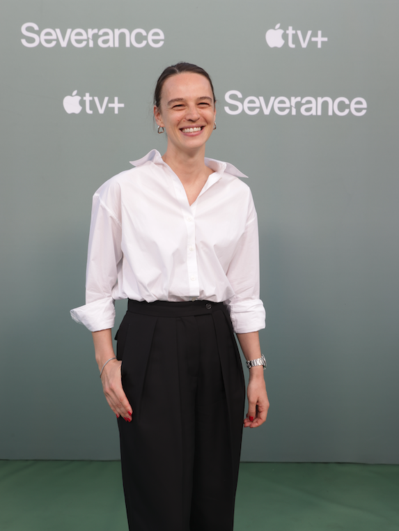 A woman posing on a green carpet in front of a backdrop that reads "Severance Apple TV+"