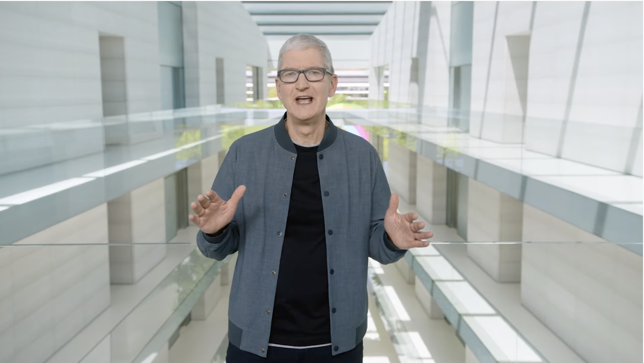 Tim Cook is wearing a black shirt, gray bomber, and grey glasses.