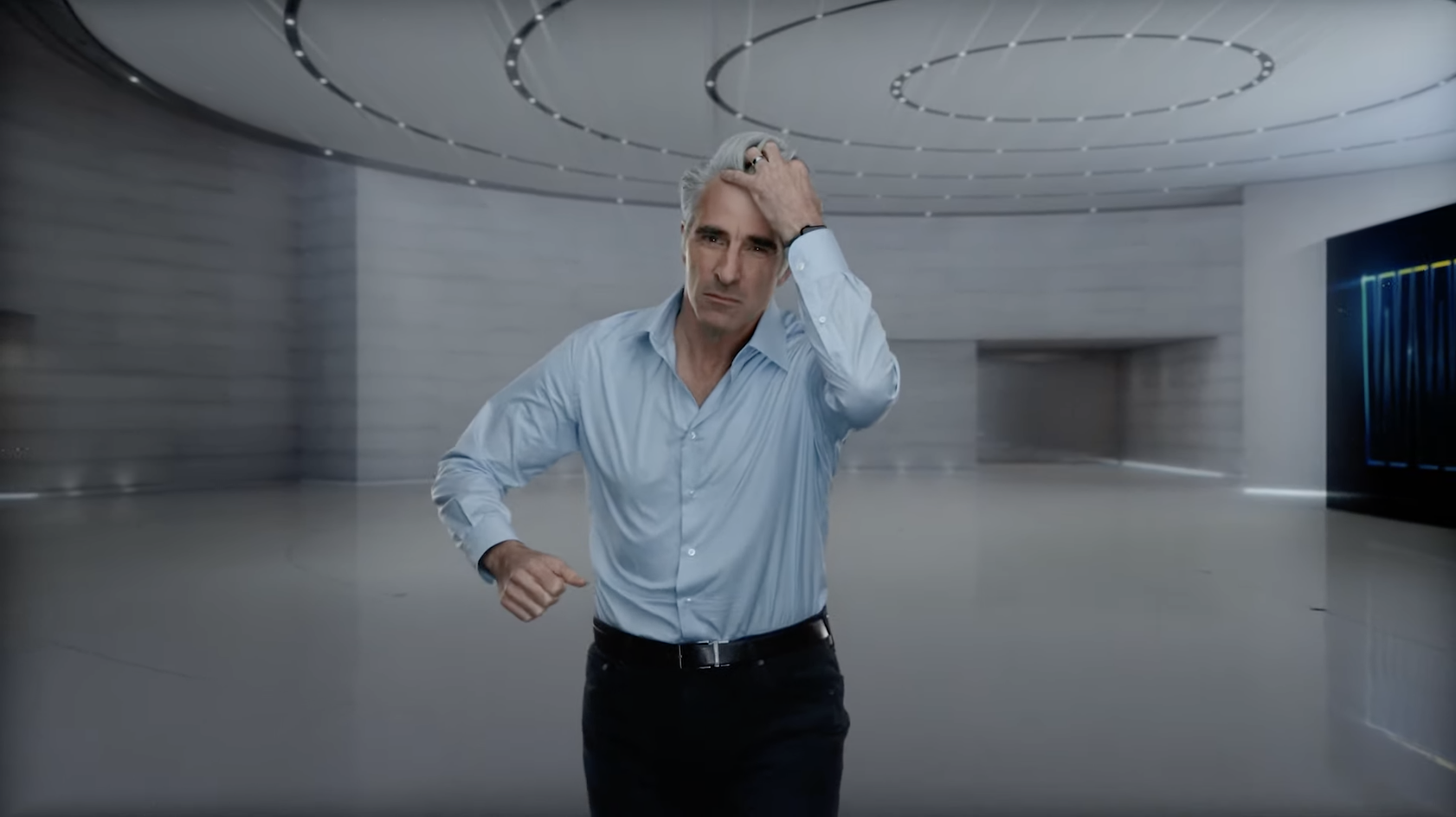 Craig Federighi swipes a hand through his grey hair. he is wearing a blue button up and black slacks.