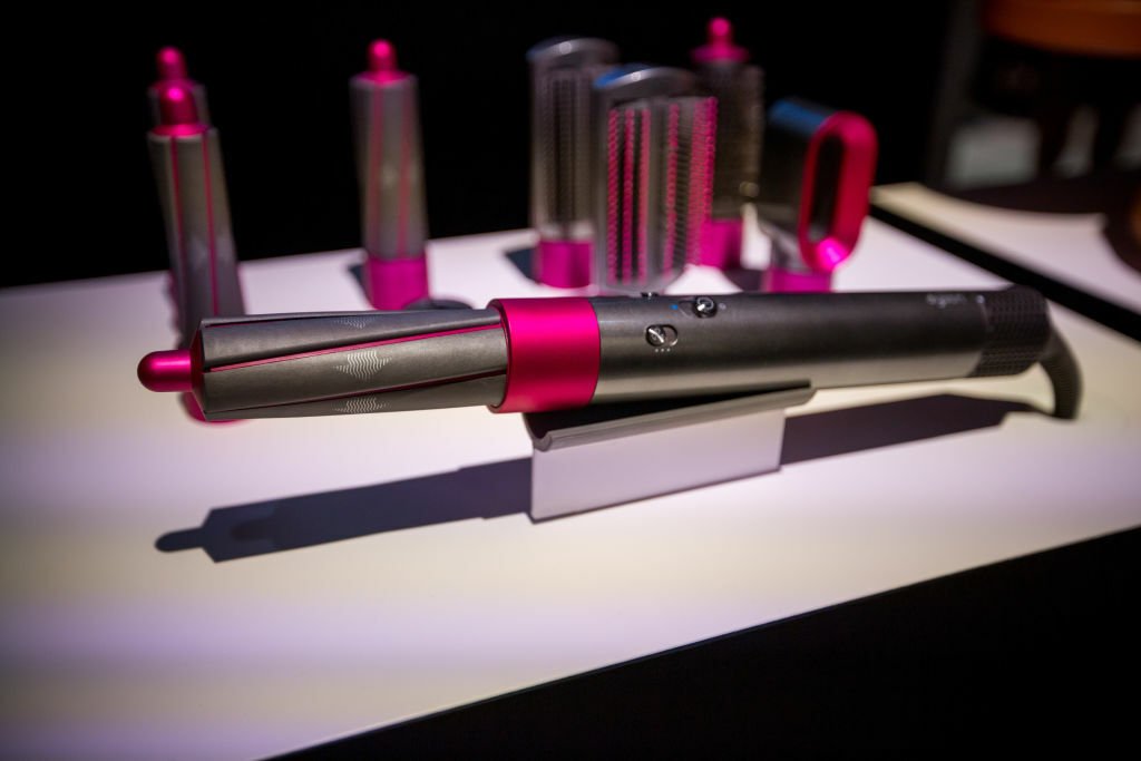 Pink and gray Airwrap device with the curling barrel attached, other attachments sit in background. 