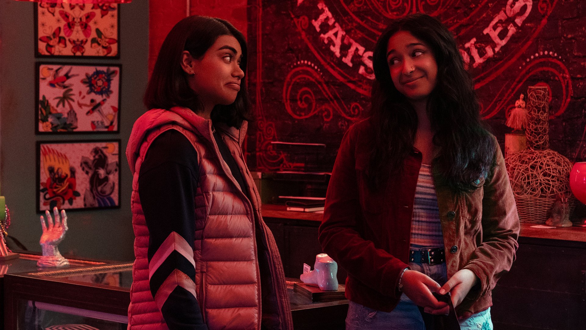 Two girls smile at each other in a tattoo parlour.