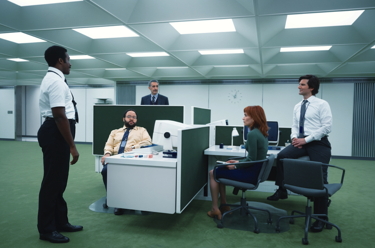 Four men and a woman gathered around desks in an office.