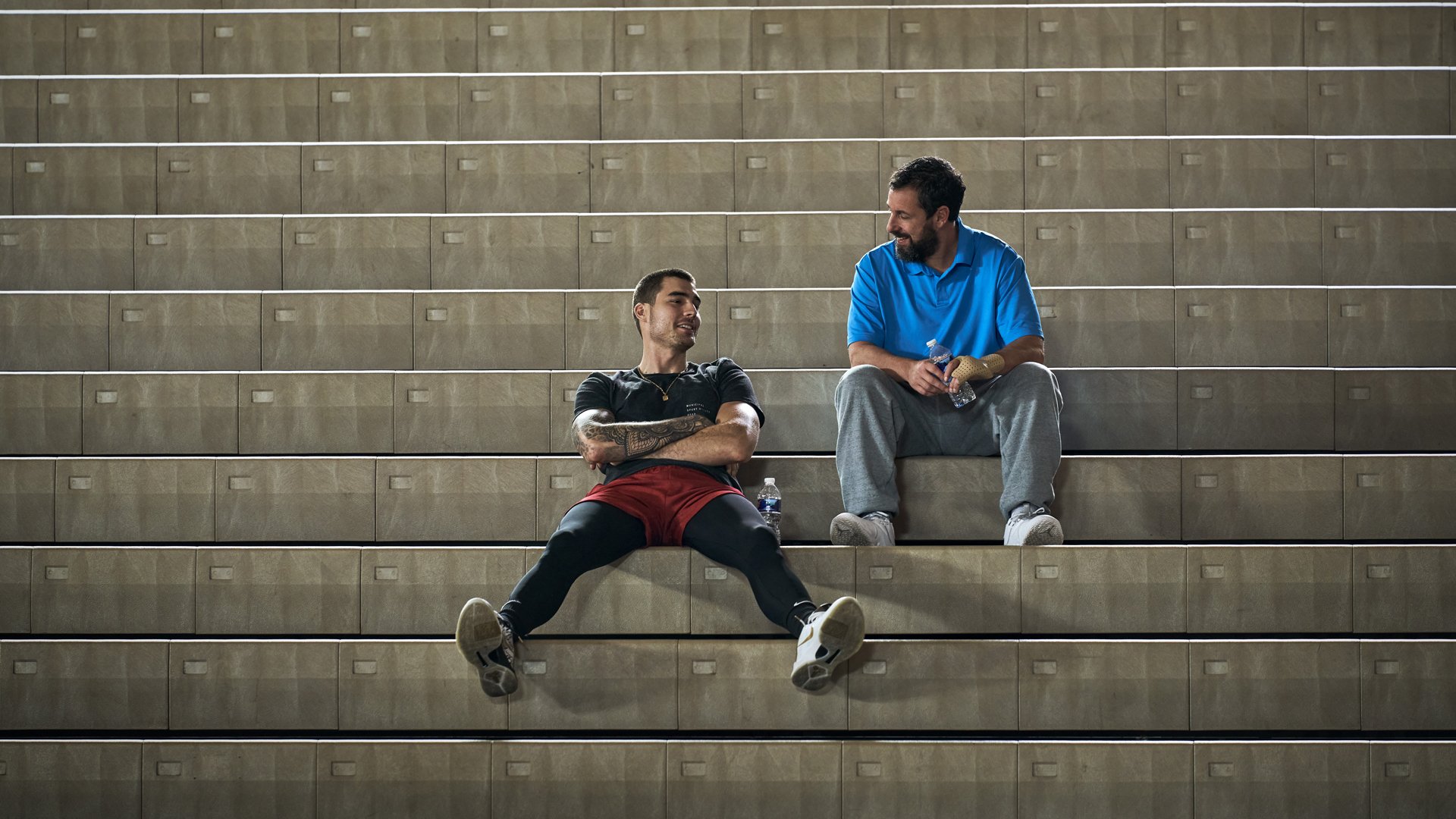 Two men sit in a basketball grandstand.