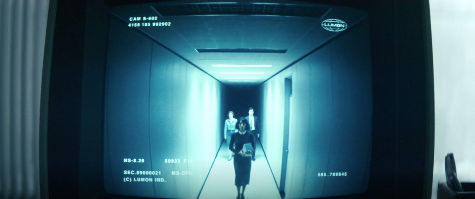 A TV screen showing security footage of three people walking down a hallway.