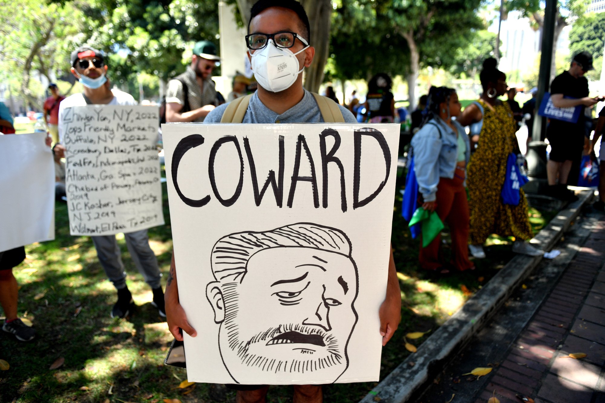 protestor holds sign with drawing of senator ted cruz with 'coward' written above