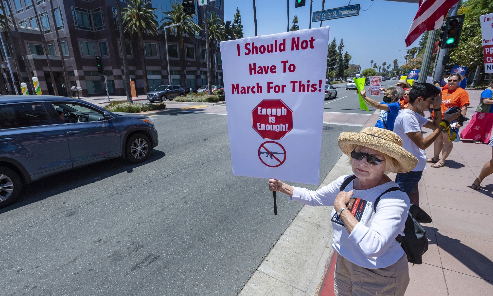 woman in hat holds sign that reads 'i should not have to march for this. enough is enough' on sidewalk