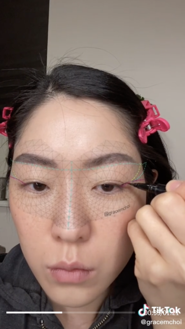 Asian woman with dark hair looks at camera and applies eyeliner with a filter overlaid.