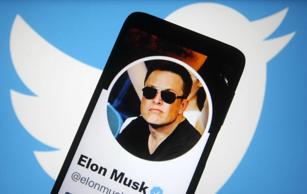 Image of Elon Musk's Twitter profile on a phone agains the background of the twitter logo