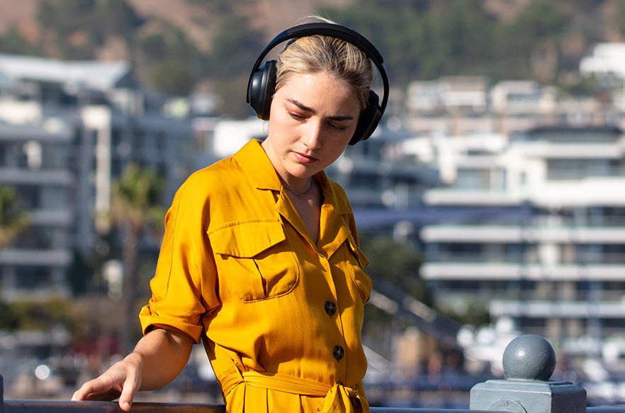 Woman outside wearing yellow dress listening to Bose 700 wireless headphones