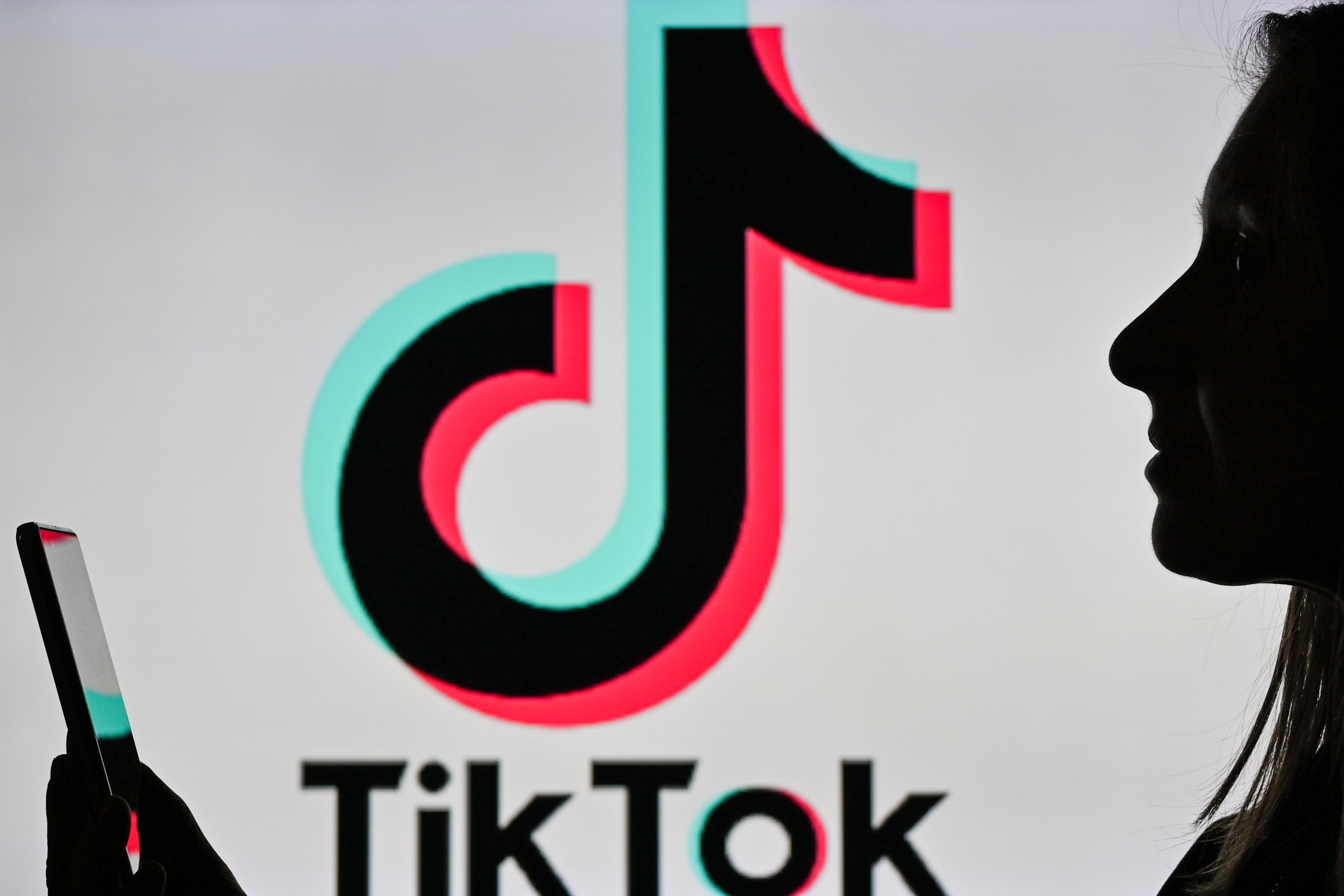 A person with a smartphone silhouetted against the TikTok logo.