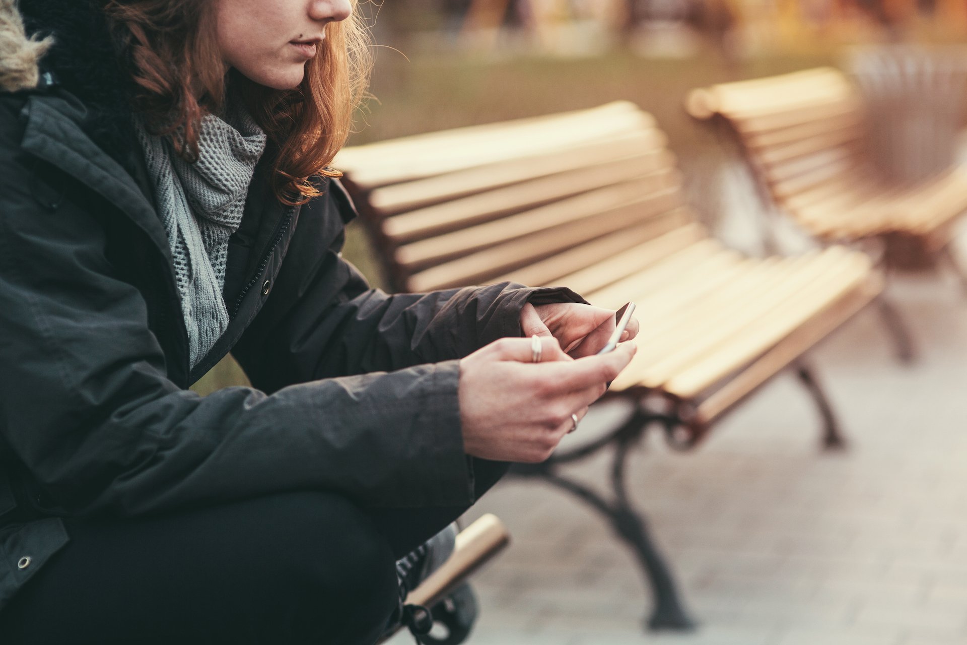 A woman sits on a bench and looks down at her phone. 