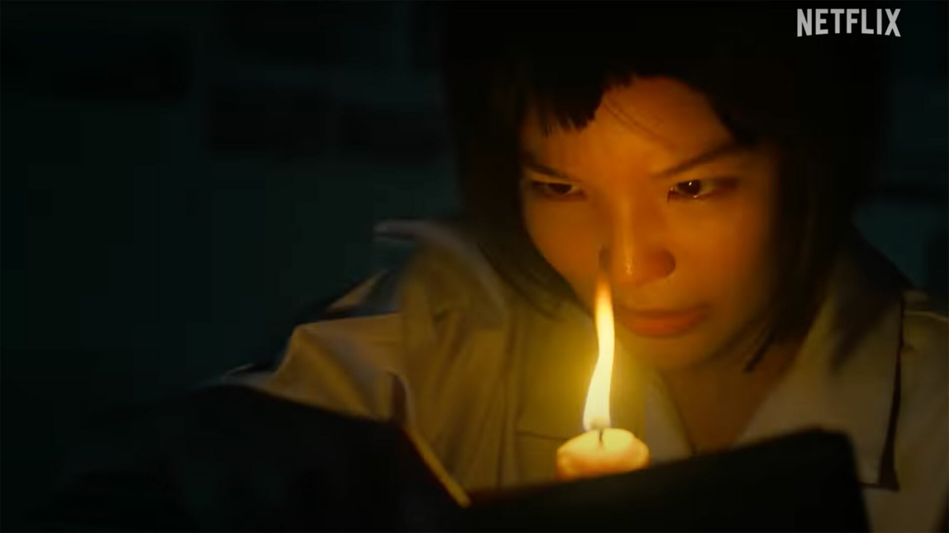 A student reads a book by candle light in the dark