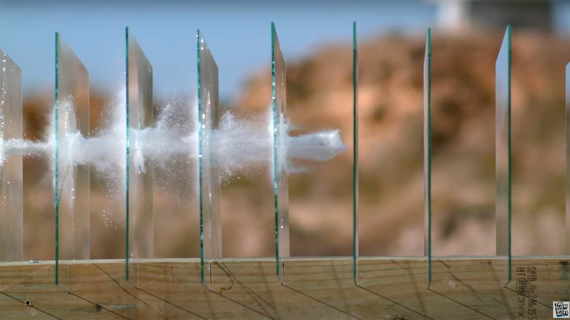 A bullet pass through multiple panes of glass in slow motion, leaving a trail behind it