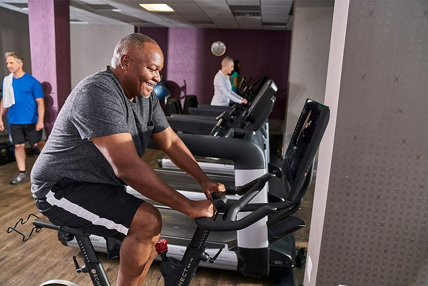 Man working out on Echelon EX-7s smart indoor bike in a gym next to treadmills.