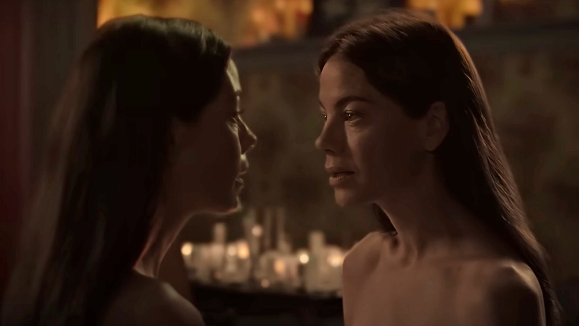 Two identical twin women stare at each other in a candlelit room.