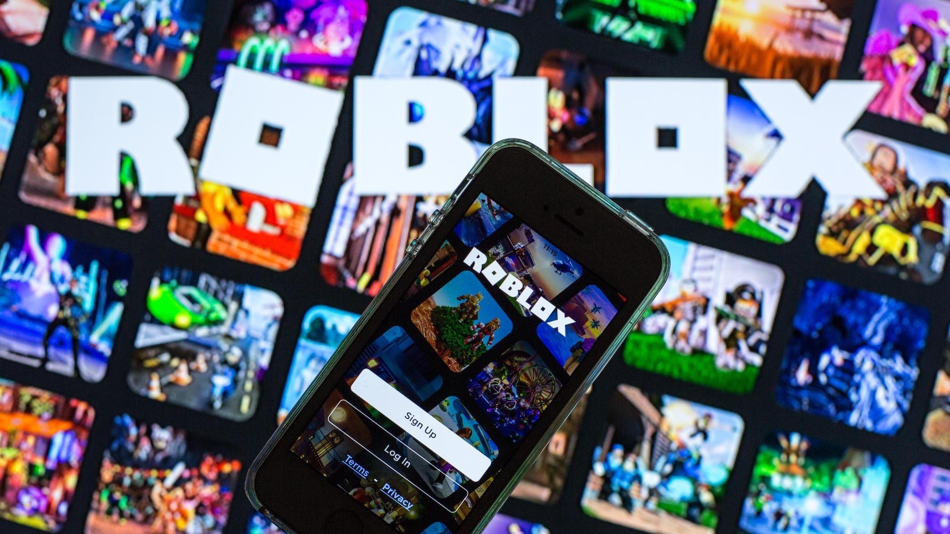 In this photo illustration, the Roblox app seen displayed on a smartphone screen and a Roblox logo in the background.