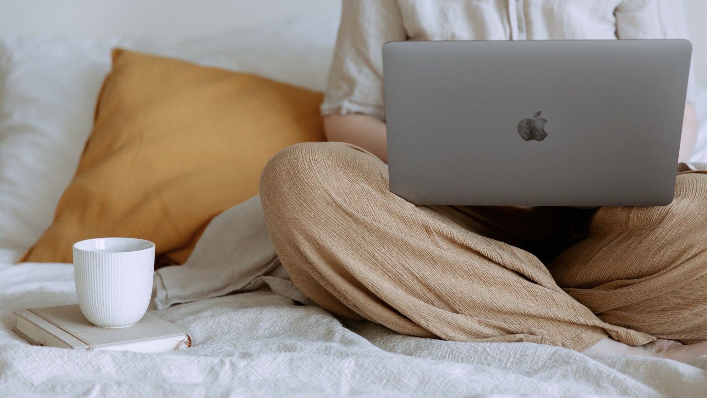 Person sitting on a bed on their laptop.