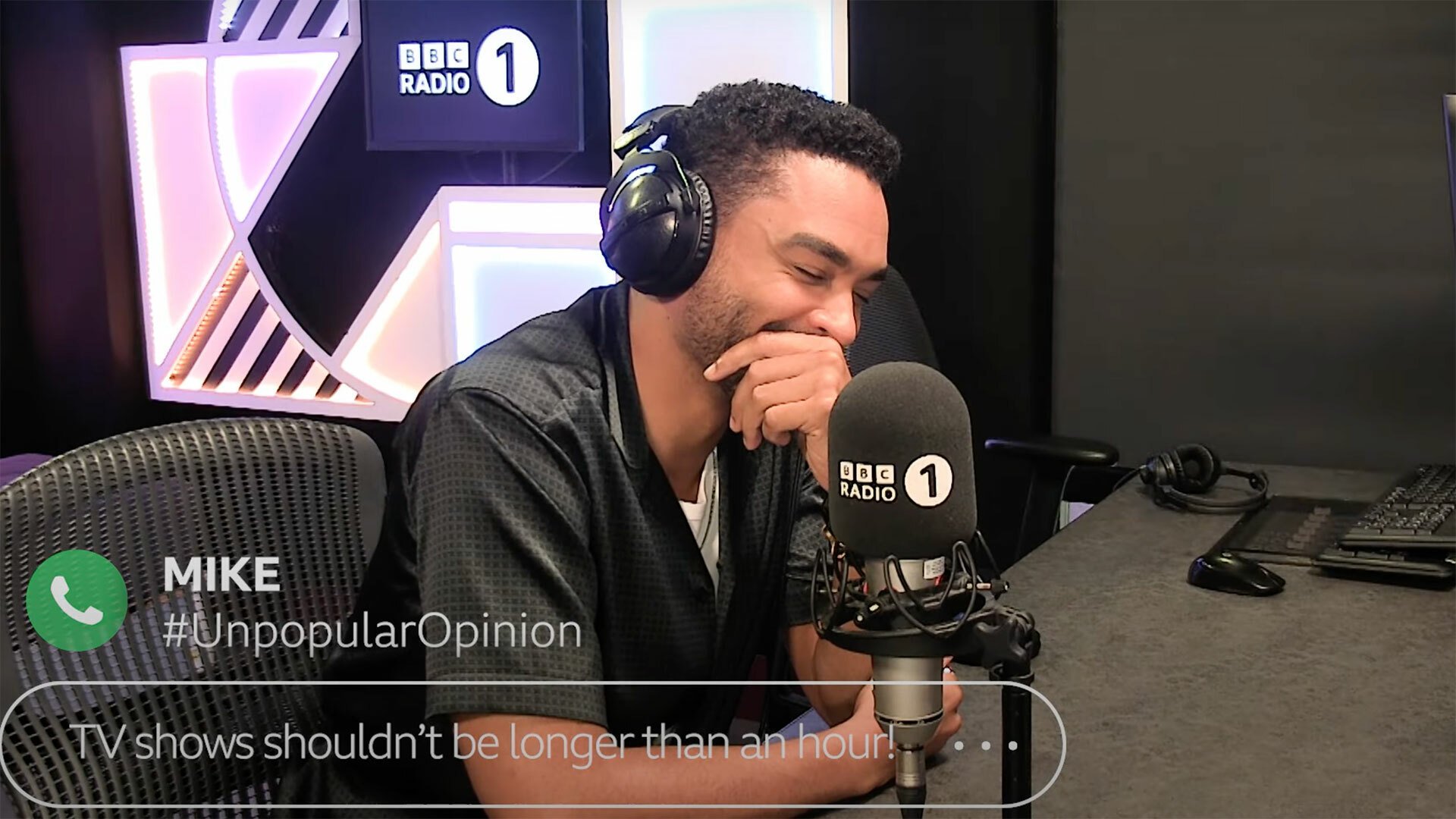 A man in a radio studio wearing headphones laughs wearily.