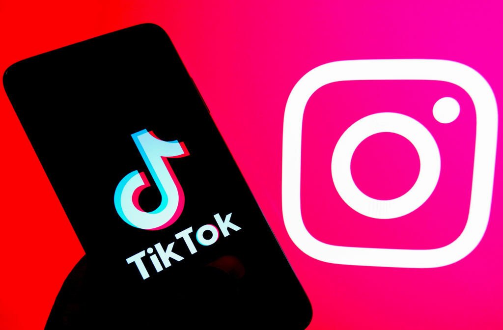 A Tiktok logo seen displayed on an android smartphone with an Instagram logo in the background.