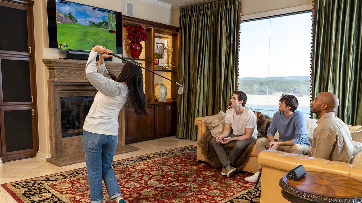 Person swinging golf club with golf scene on TV while other people watch from sofa
