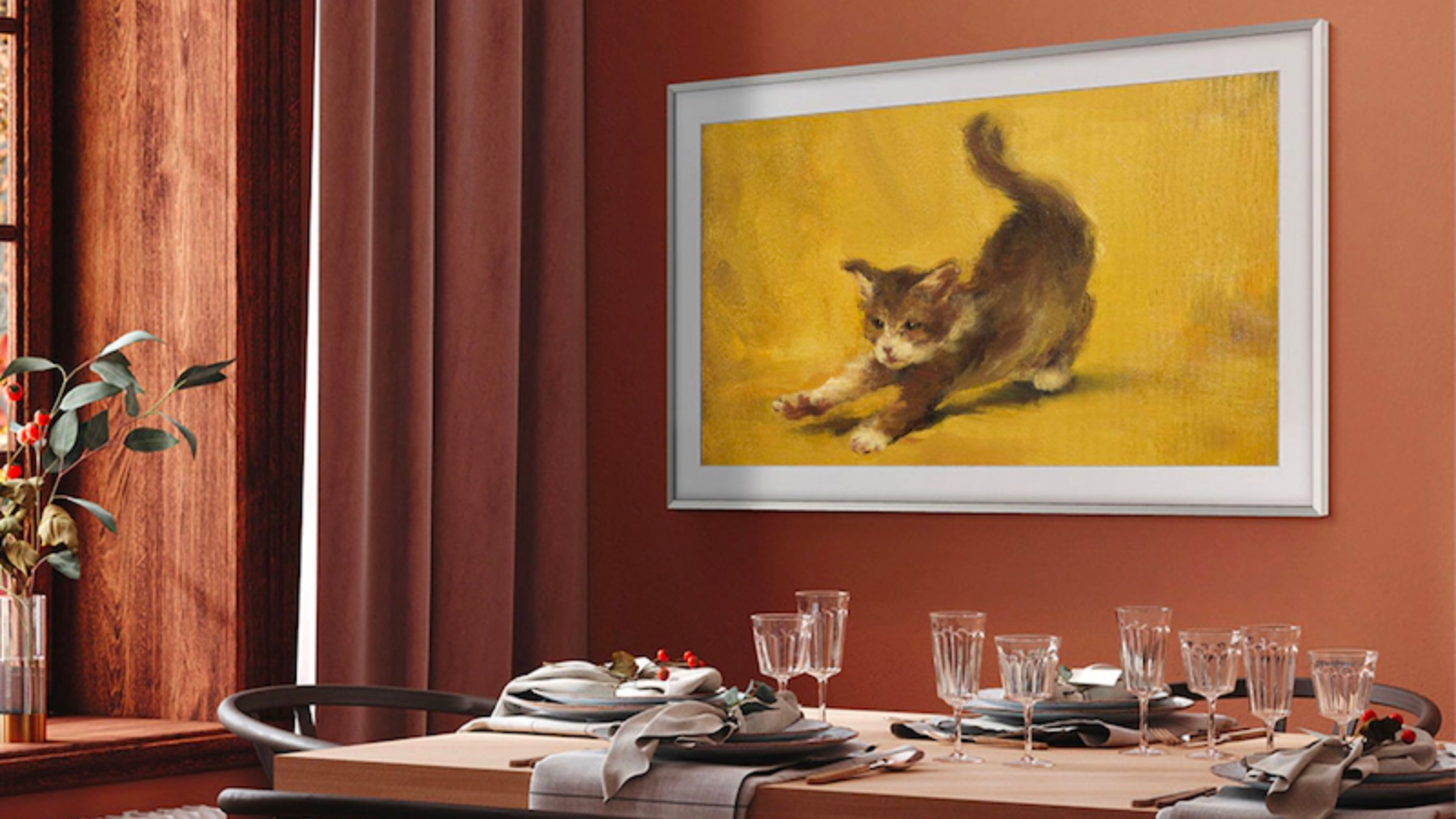 a samsung the frame tv displaying.a picture of a stretching kitten hangs on an orange wall above a set dinner table